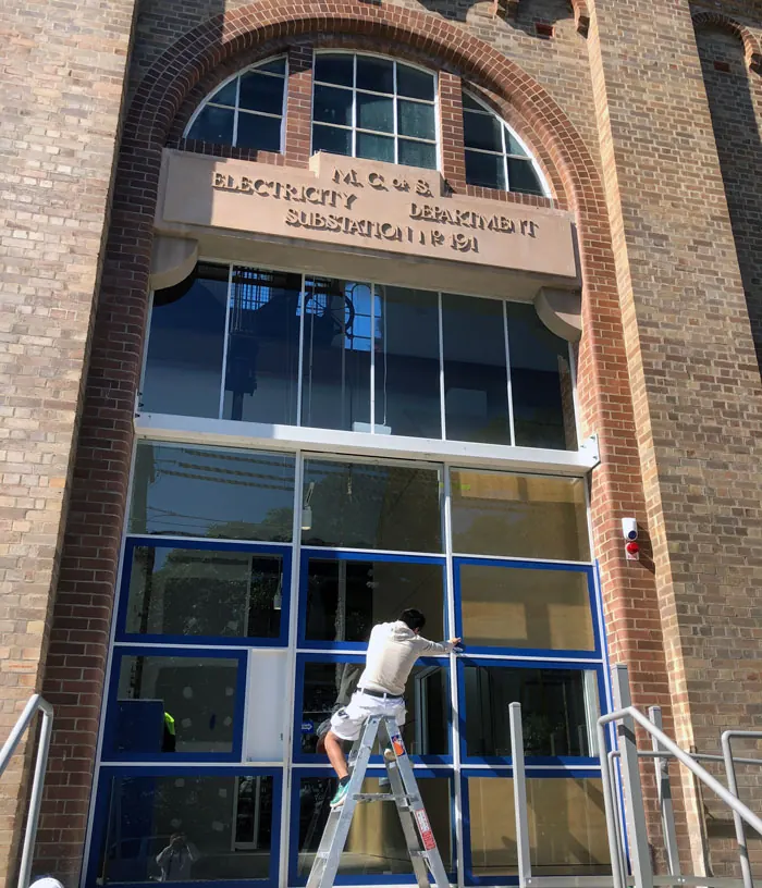 Painter on a stepladder at the arched entrance of a heritage brick building with a sandstone lintel