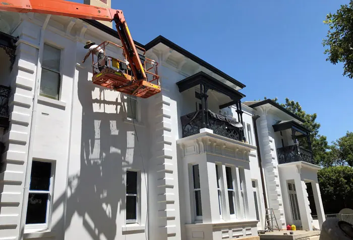 Painter in a boom lift working on the render of a heritage villa